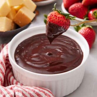 A bowl of chocolate fondue with a strawberry dipped and lifted up from it.