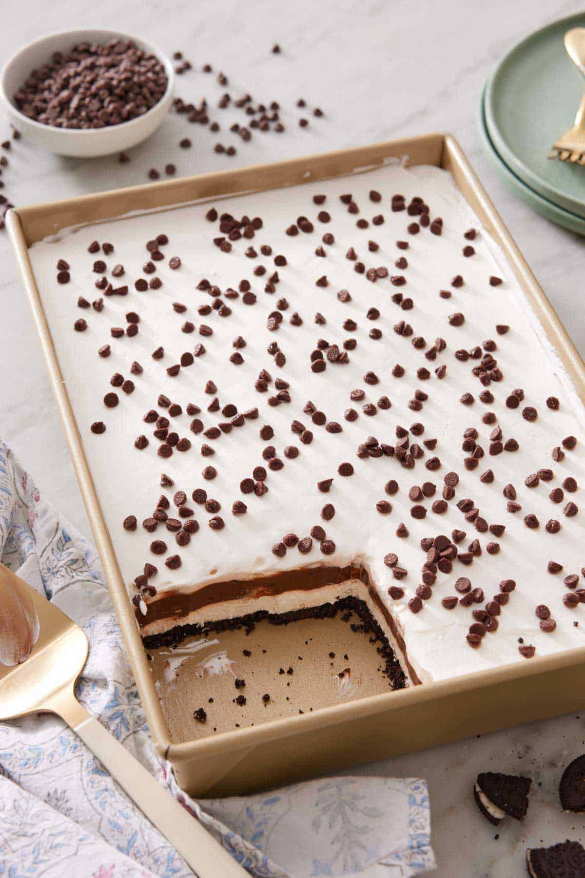 A rectangular pan of chocolate lasagna with a slice taken out. A bowl of chocolate chips in the background.