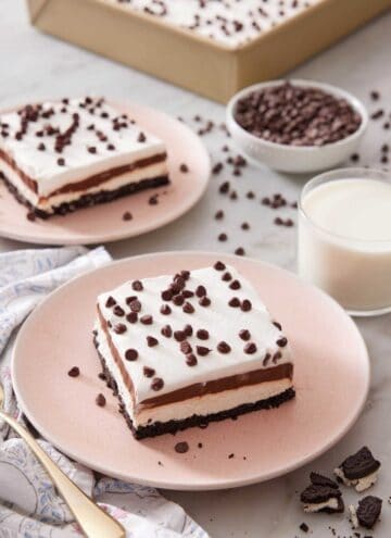 Two plates with sliced chocolate lasagna with a glass of milk, bowl of mini chocolate chips, and a pan of more chocolate lasagna in the background.