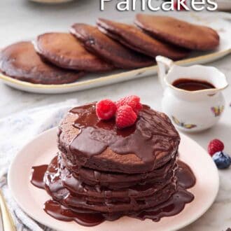 Pinterest graphic of a plate with a stack of chocolate pancakes with chocolate sauce and topped with raspberries. More pancakes and sauce in the background.