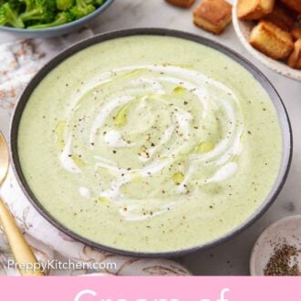 Pinterest graphic of a bowl of cream of broccoli soup with cream swirled on top with pepper. Broccoli, shredded cheese, and croutons in the background.