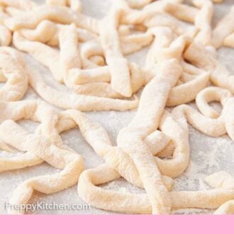 Pinterest graphic of strands of uncooked egg noodles tossed in flour on a counter.