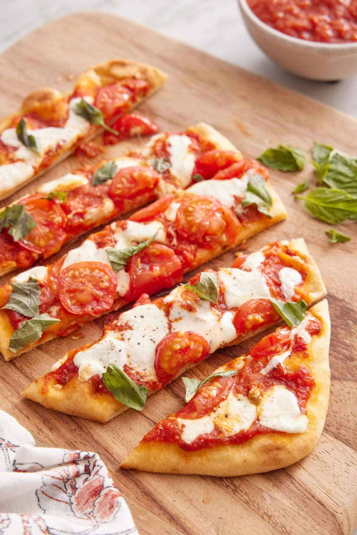 A cutting board with a cut flatbread pizza with some basil.