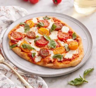 Pinterest graphic of a plate with a flatbread pizza topped with fresh basil. Tomatoes and a glass of wine in the background.