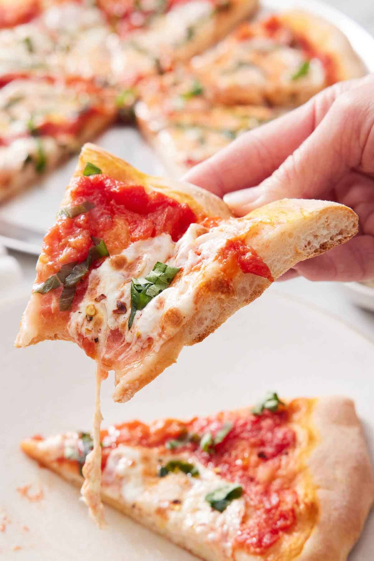 A slice of margherita pizza with a large bite taken out with more slices in the background.