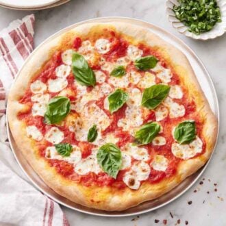 Overhead view of a margherita pizza topped with fresh basil with some red pepper flakes scattered around and more basil to the side.
