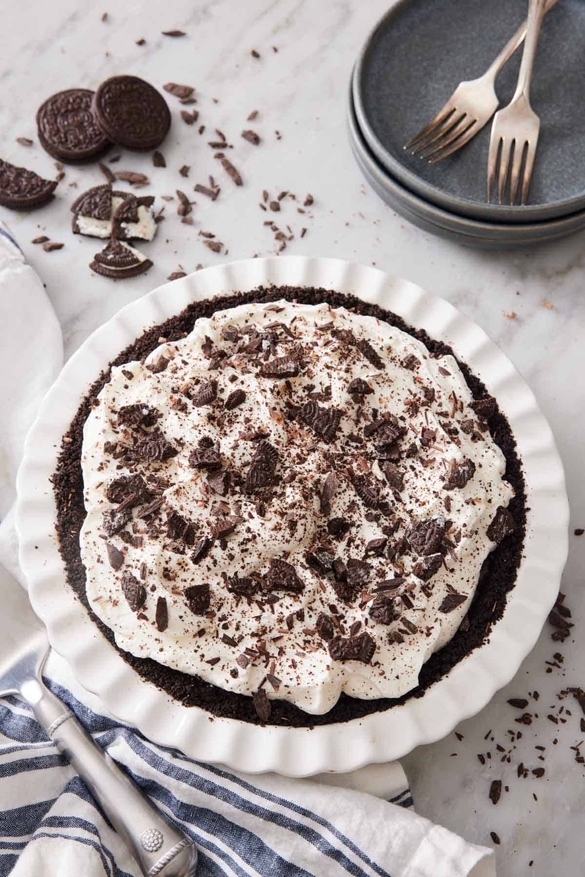 Overhead view of a mud pie in a white baking dish. Oreos, stacks of plates, and forks in the background.