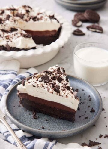 A slice of mud pie on a plate with a glass of milk and the rest of the pie behind it.