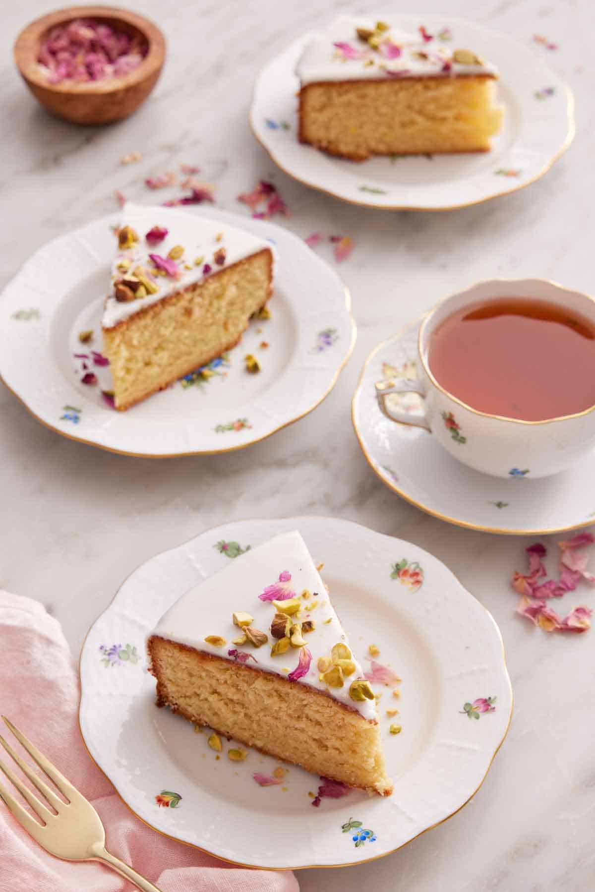 Three plates with sliced Persian love cakes and a cup of tea off to the side with some dried rose petals.