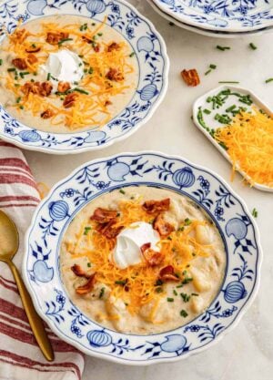 Two bowls of potato soup with shredded cheese, bacon, sour cream, and chives on top.