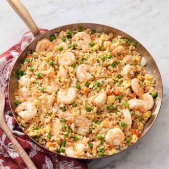 Overhead view of a skillet of shrimp fried rice with a wooden spoon beside it.