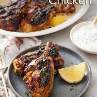 Pinterest graphic of a plate with two pieces of tandoori chicken with a lemon wedge with a yogurt sauce in the background with the rest of the chicken on a platter.