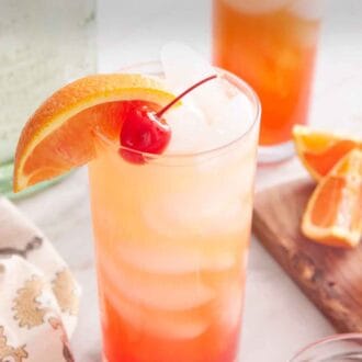 Pinterest graphic of a glass of tequila sunrise with an orange slice and maraschino cherry as garnish. A second glass in the background along with the cut orange slices and tequila bottle.
