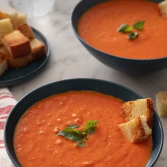 Pinterest graphic of two bowls of tomato soup topped with some bread and fresh basil.