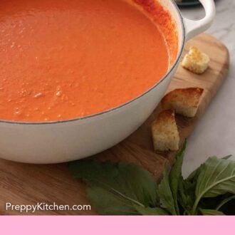 Pinterest graphic of a white pot containing tomato soup. Basil and toasted beard scattered around.