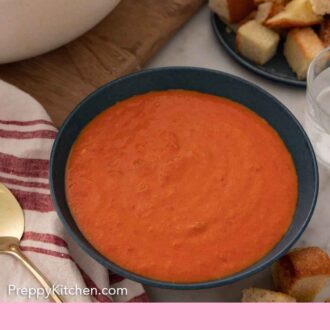 Pinterest graphic of a bowl of tomato soup with a pot and plate of toasted bread in the back.