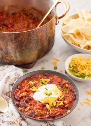 A bowl of turkey chili with bowls of toppings and a pot of more chili with a ladle in the background.