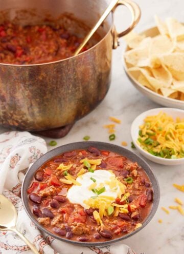 A bowl of turkey chili with bowls of toppings and a pot of more chili with a ladle in the background.
