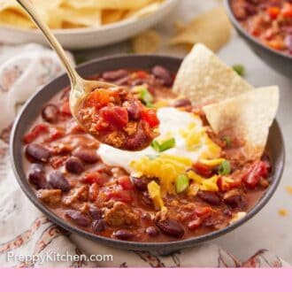 Pinterest graphic of a spoonful of turkey chili lifted out of the bowl with a plate of chips in the background.