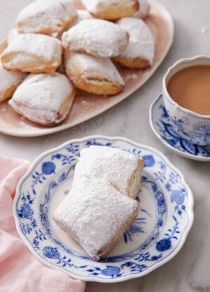A plate with two air fryer beignets with a platter in the background along with a cup of coffee.