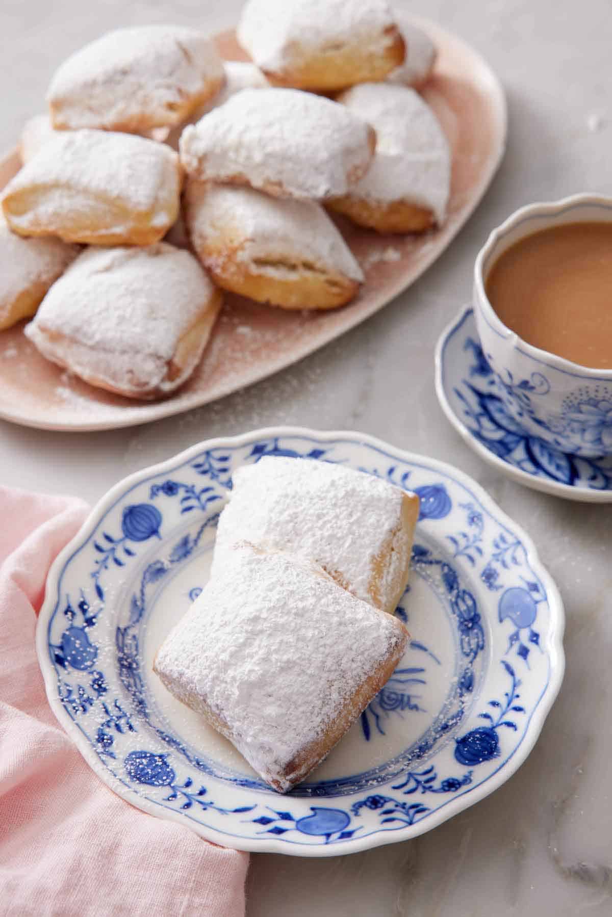 A plate with two air fryer beignets with a platter in the background along with a cup of coffee.