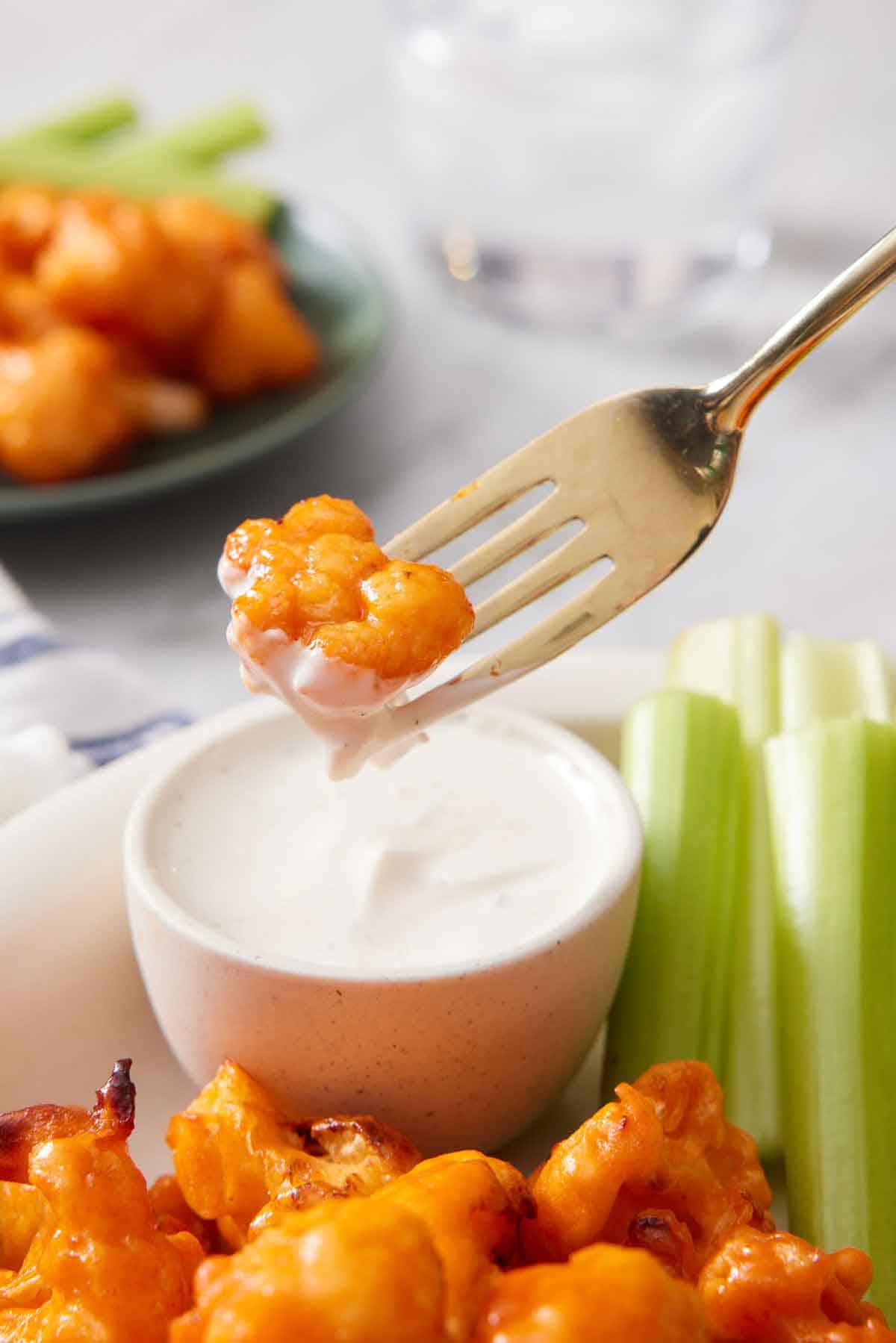 An air fryer buffalo cauliflower on a fork, dipped into a bowl of sauce and lifted up.