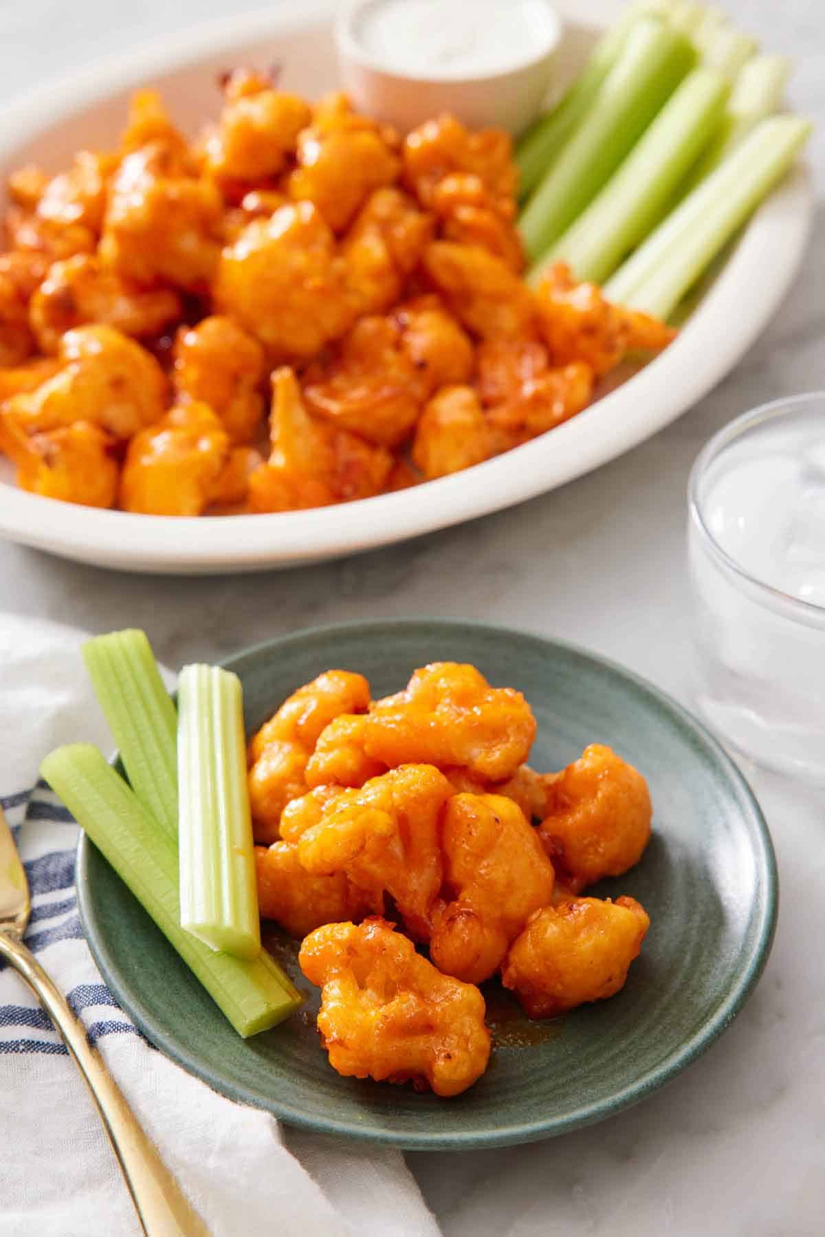 A plate with air fryer buffalo cauliflower and celery sticks with more on a platter in the background.
