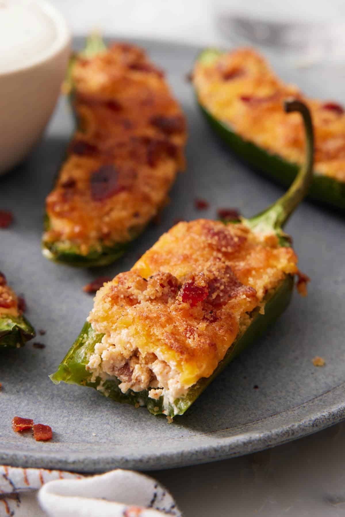 A close up view of air fryer jalapeno poppers on a plate with one with a bite taken out of it.