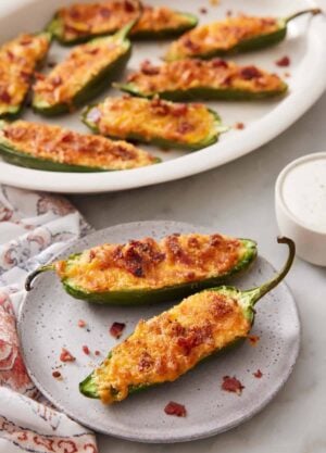 A plate with two air fryer jalapeno poppers with more in a platter in the background.