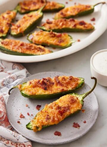 A plate with two air fryer jalapeno poppers with more in a platter in the background.