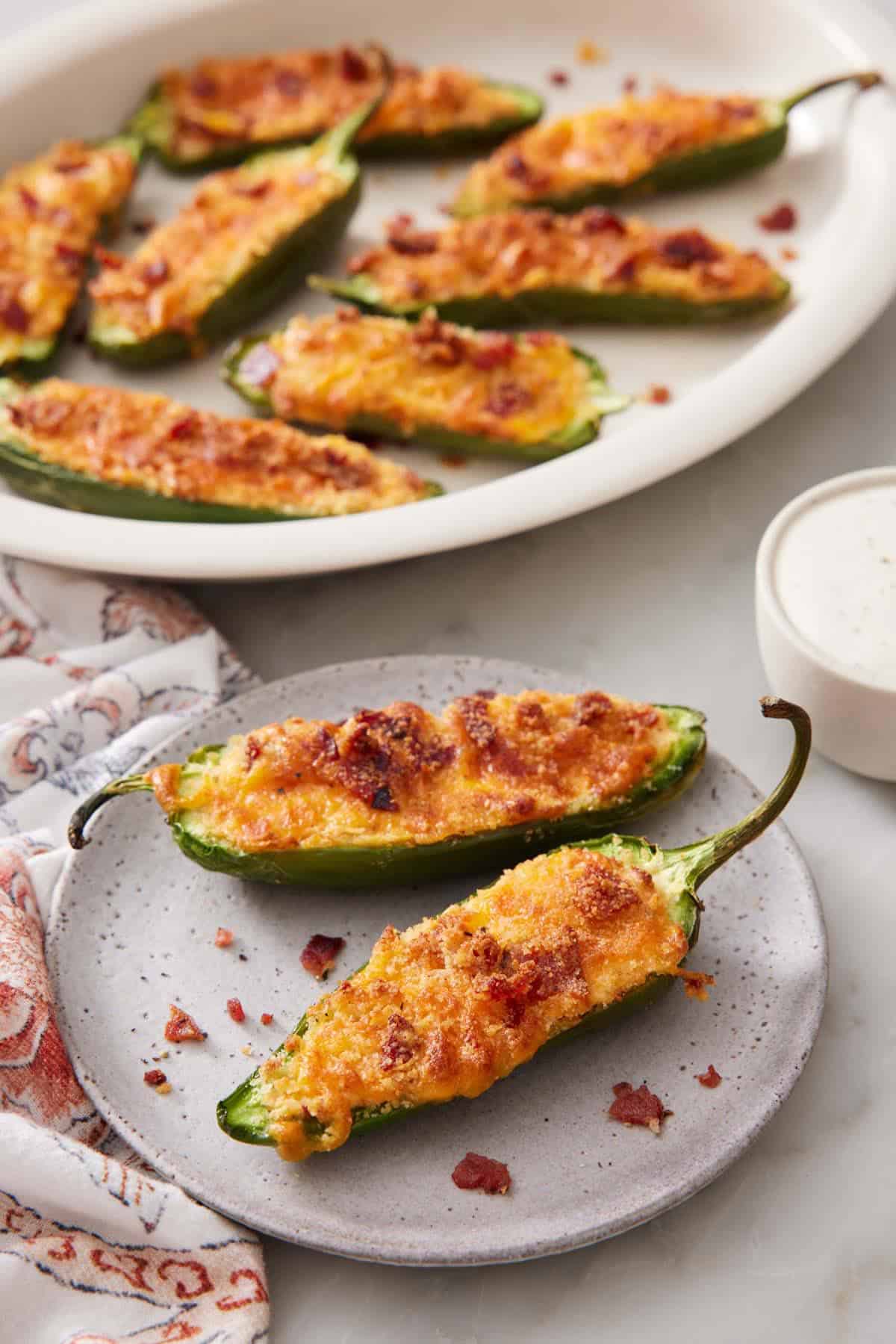 A plate with two air fryer jalapeno poppers with more in a platter in the background.