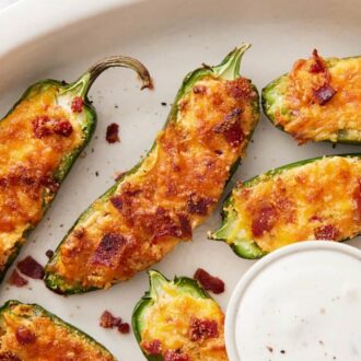 Overhead view of multiple air fryer jalapeno poppers on a platter with a bowl of dipping sauce.
