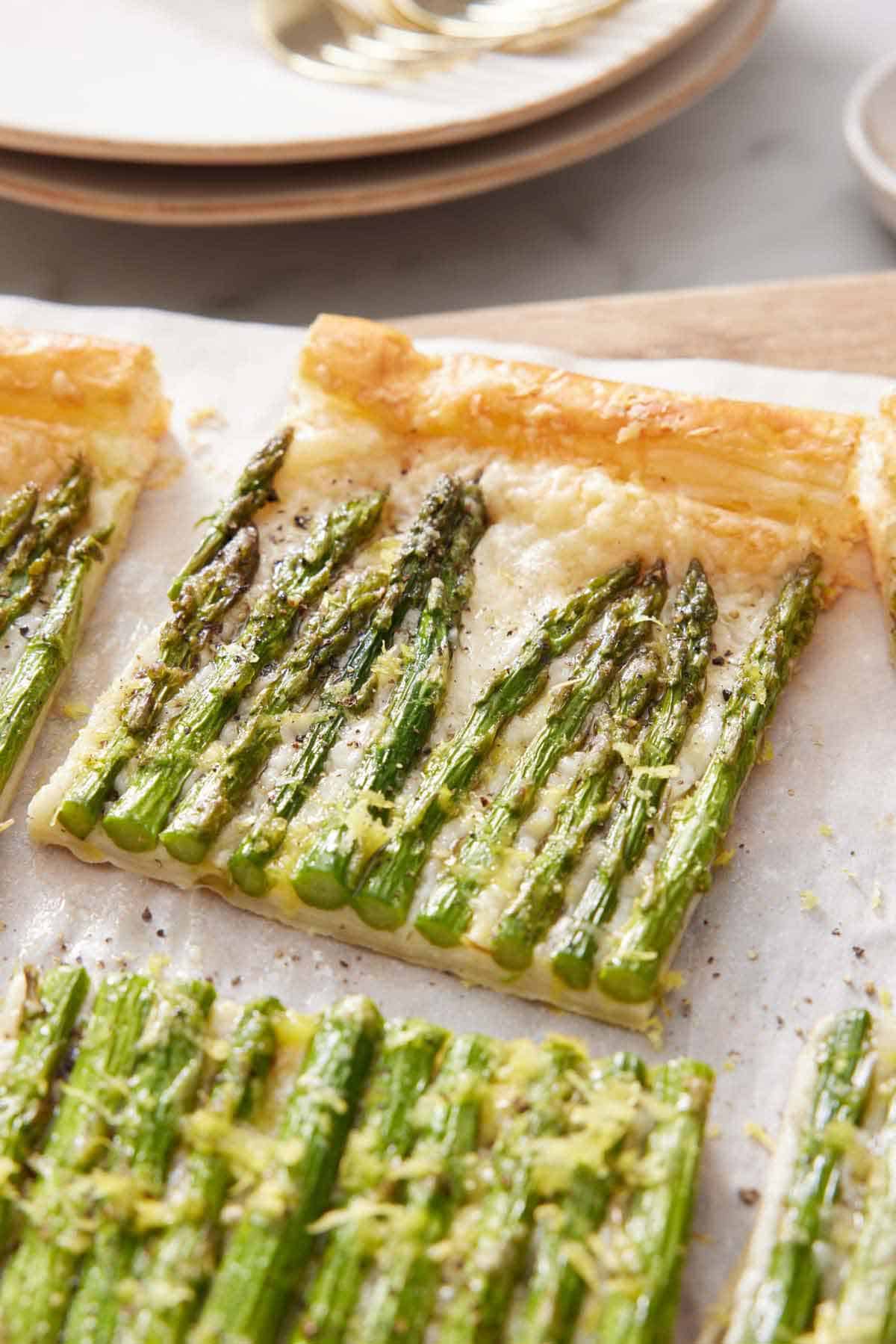 A slice of asparagus tart slightly pulled away from the rest of the tart on a sheet of parchment.