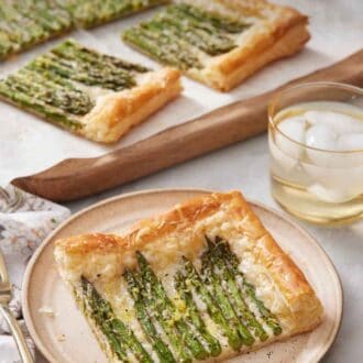 Pinterest graphic of a plate with a slice of asparagus tart with the rest in the back on a serving board along with a drink.