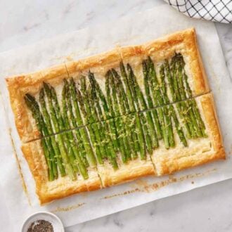 Overhead view of an asparagus tart on a sheet of parchment with a bowl of pepper.