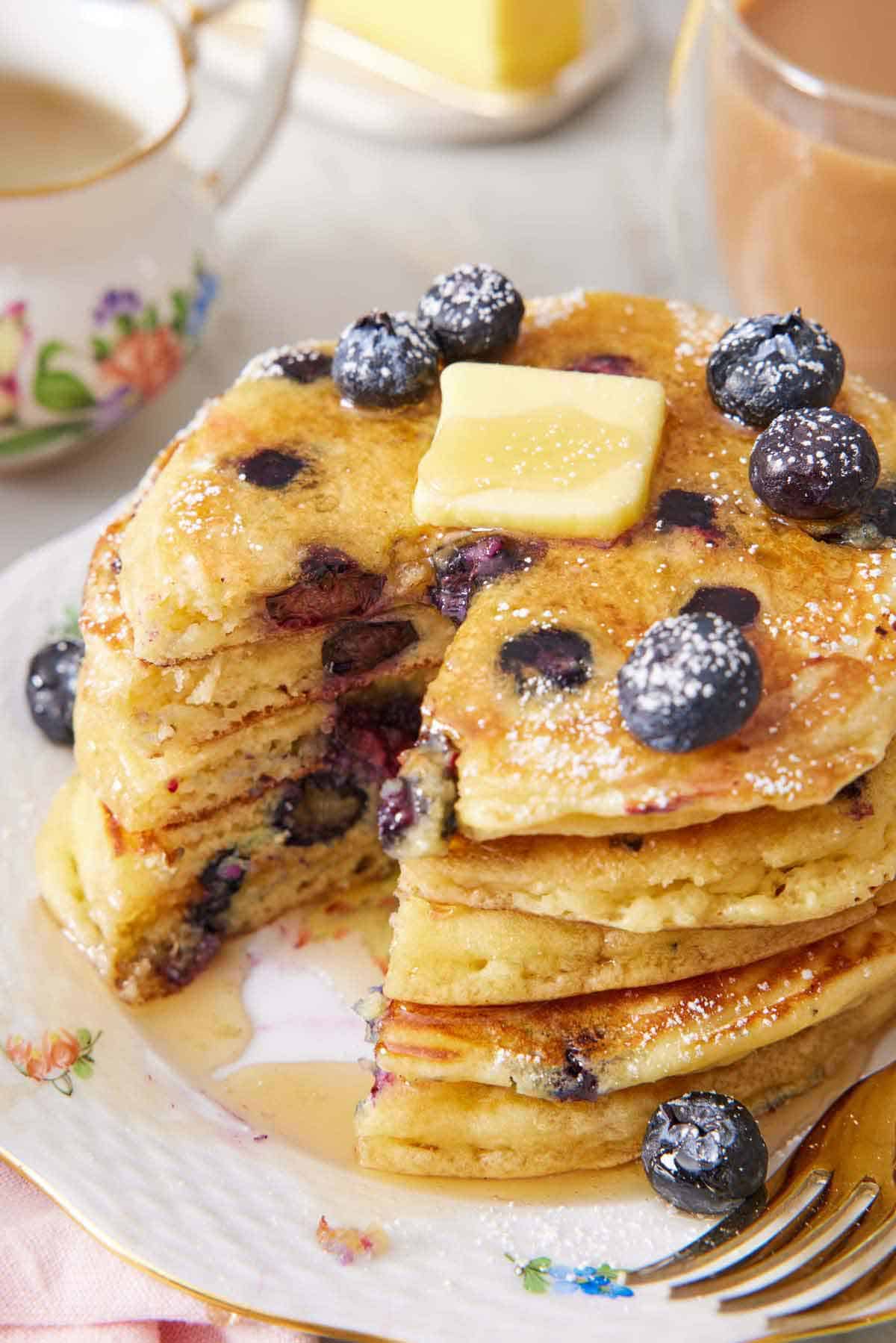A stack of blueberry pancakes with butter on top with a bite cut out.