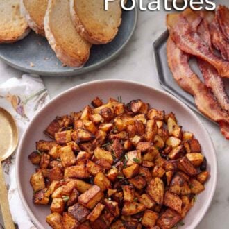 Pinterest graphic of a plate with breakfast potatoes topped with chopped rosemary. A plate of toast and bacon in the back.