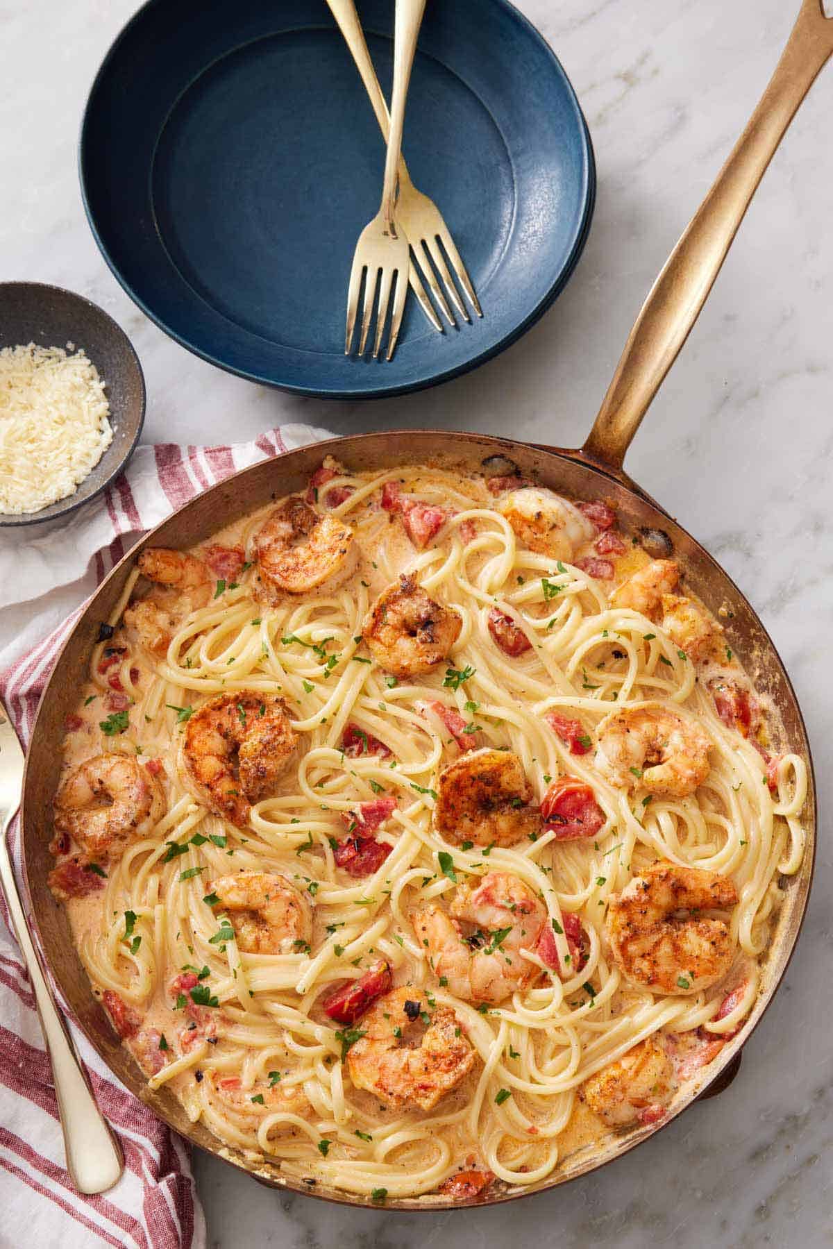 Overhead view of a skillet of cajun shrimp pasta. A plate with two forks beside it.