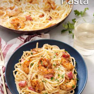 Pinterest graphic of a plate of cajun shrimp pasta with chopped parsley garnish with a skillet with more pasta in the background.