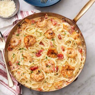 An overhead view of cajun shrimp pasta in a skillet with a fork and bowl of parmesan on the side.