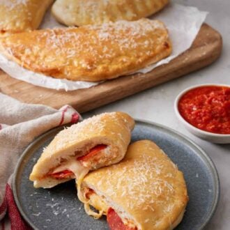 Pinterest graphic of a plate with a calzone cut in half, showing the interior. More calzones in the background along with a bowl of sauce.