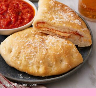 Pinterest graphic of a plate with a calzone cut in half with one half slightly propped on top of the other, showing the interior. A bowl of pizza sauce on the side.