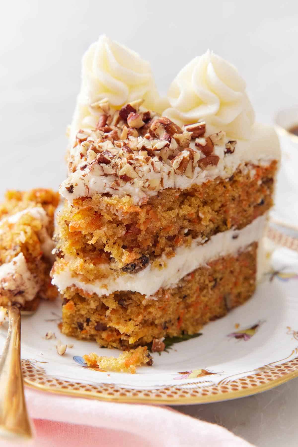 A slice of carrot cake on a plate with the tip on a fork beside it.