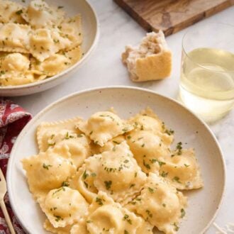 Pinterest graphic of a plate of cheese ravioli. Behind it is a glass of wine, torn bread, and another plate of ravioli.