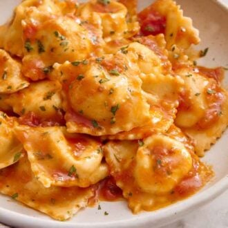A plate of cheese ravioli tossed in a tomato sauce and garnished with chopped herbs.