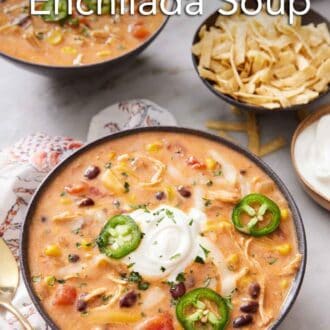 Pinterest graphic of two bowls of chicken enchilada soup topped with sliced jalapeno with a bowl of tortilla strips on the side.