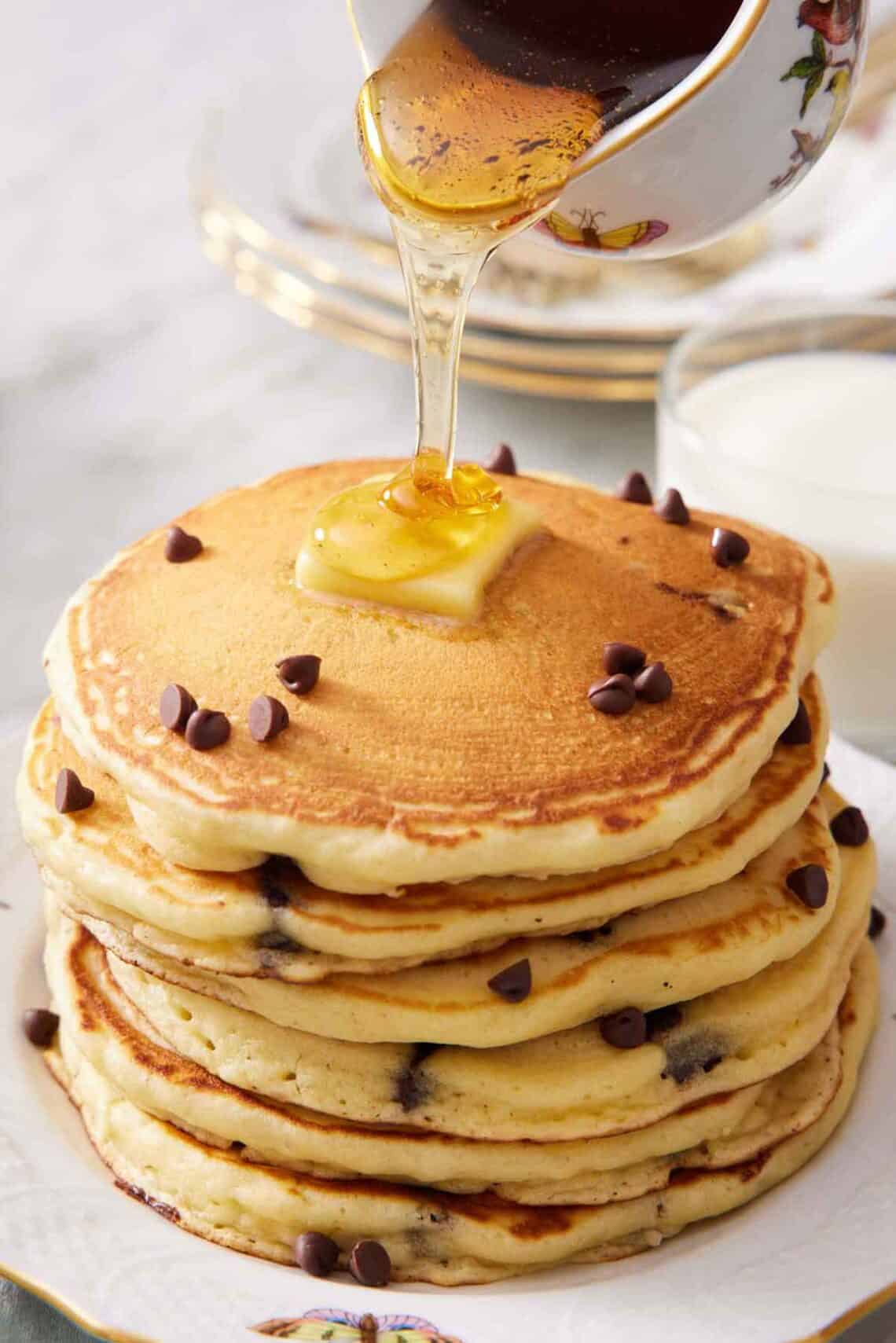 Syrup poured over a stack of chocolate chip pancakes with butter.