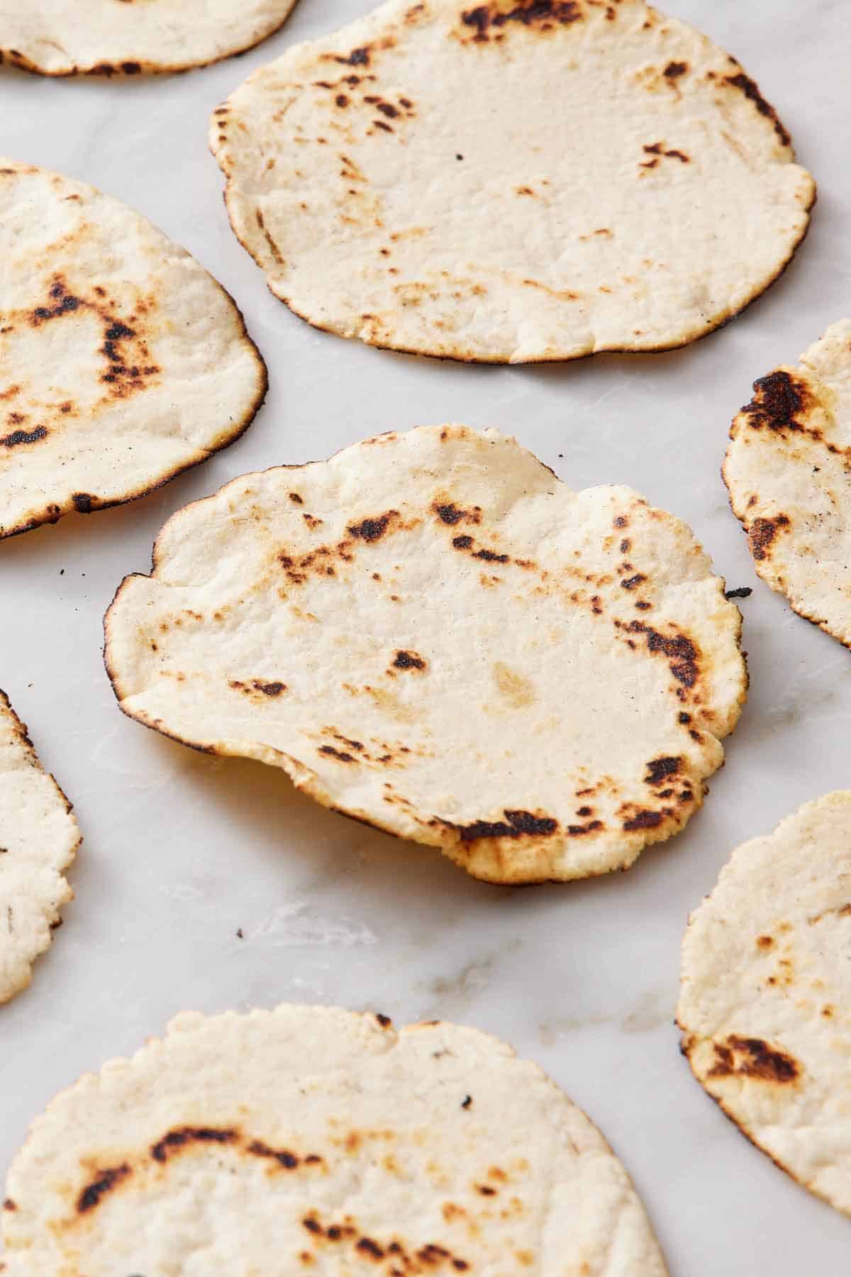 Multiple corn tortillas in a single layer on a marble surface.
