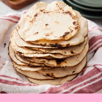 Pinterest graphic of a stack of corn tortillas on a linen napkin with a stack of plate in the background along with sliced jalapenos and limes.