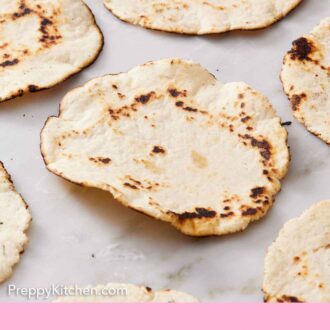 Pinterest graphic of multiple corn tortillas in a single layer on a marble surface.